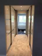 Wardrobes on both sides of a corridor between the bedroom and ensuite with end door open